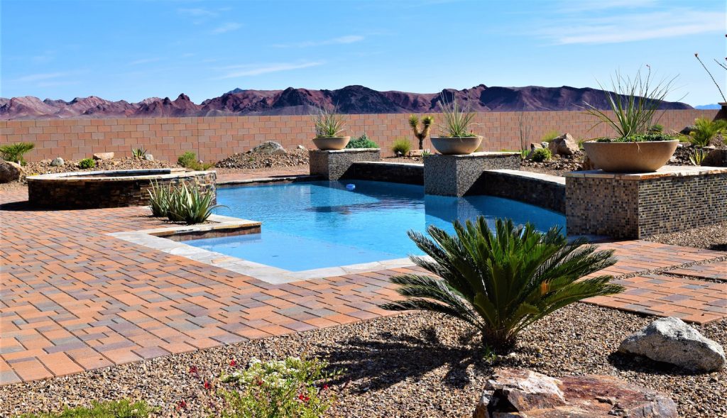 A pool with a brick patio and plants in the background. A pool with a brick patio and plants in the background.